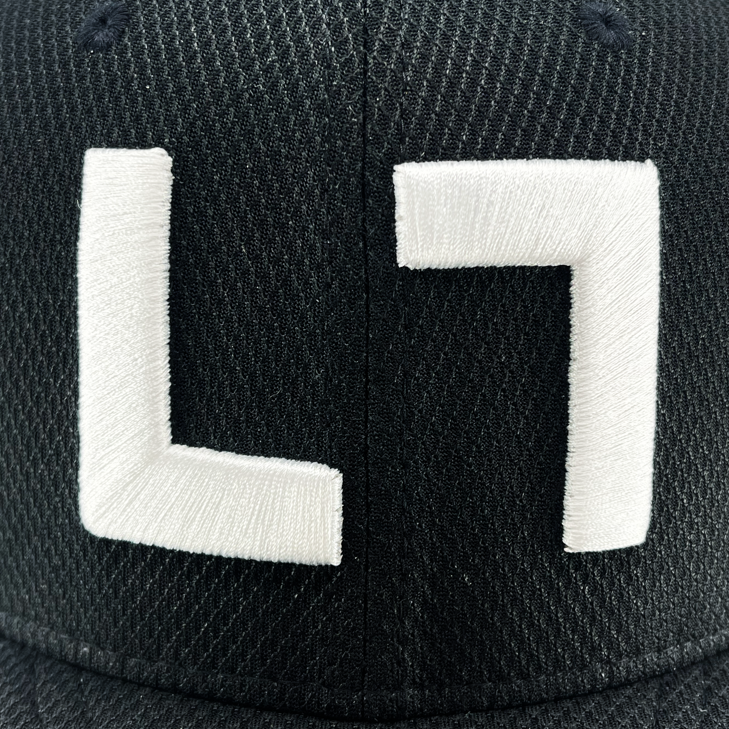 The black textured Authentic Kollection 59FIFTY Fitted cap by Kulture features bold white embroidery of symbols resembling an "L" and a rotated "L" on the front, adding a unique touch to any cap collection.