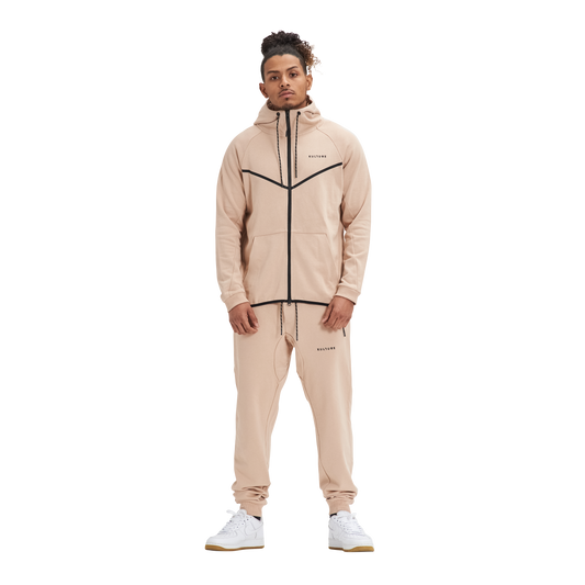 A man in Kulture's ATL Sand Full-Zip Hoodie & Joggers stands in front of a white background.